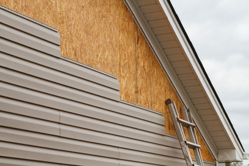 Beige siding being installed on a suburban home.