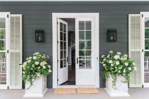 Pair of hinged patio doors with white frame and sashes on farmhouse porch with matching white-frame windows which have white shutters