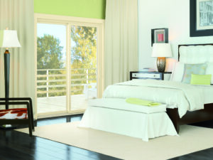 Immaculate bedroom with beige-frame sliding patio doors opening displaying view of outdoor patio and fall foliage