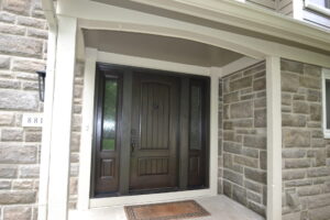 Rich, dark simulated wood door with flanking sidelights at entrance to home with stone veneer siding