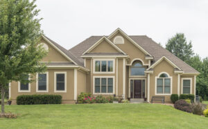 Luxury two-story home with tan siding, cream-colored window trim, and many different window styles
