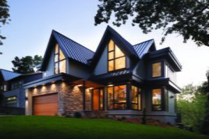 A contemporary-style, two-story home with geometrically shaped, black-frame windows, pictured at dusk with interior and exterior lights on